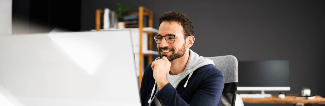 Homem sorridente observando a tela de um computador, muito provavlemente feliz que o seu site segue a diretriz Google E-E-A-T