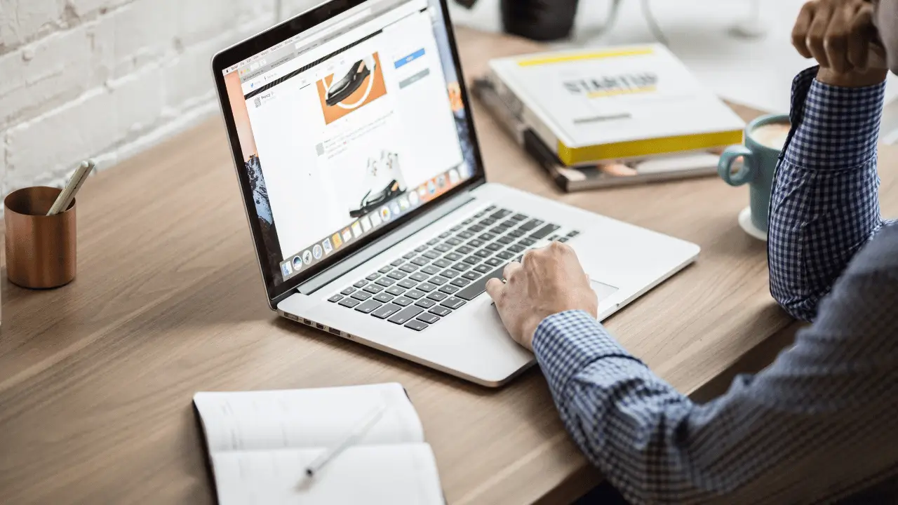 Homem mexendo em um notebook, que mostra um site na tela. O homem é branco e está vestindo uma camisa social